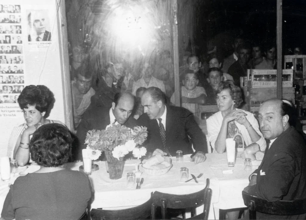 Συνεστίαση το βράδυ στο παραλιακό «Τουριστικό Περίπτερο» της Νέας Καλλικράτειας. Ο Ανδρέας Παπανδρέου συνομιλεί με τον Ιωάννη Κυριαφίνη, και δεξιά και αριστερά οι σύζυγοί τους Μαργαρίτα Παπανδρέου και Καίτη Κυριαφίνη